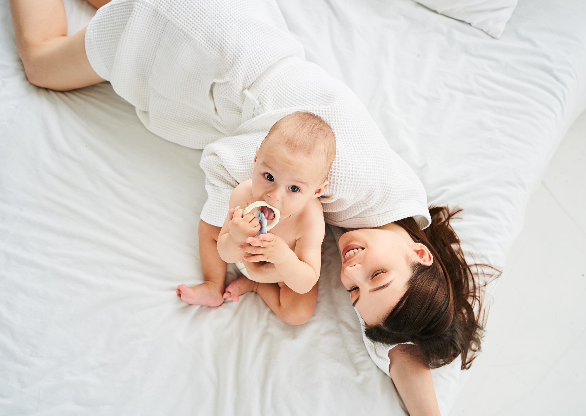 Das Bild zeigt ein Baby mit einer lachenden Mutter liegend auf einem Bett.